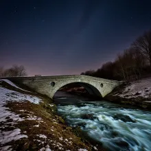 Nighttime Stone Bridge over Rapid River under Starry Sky with Milky Way Visible. Long Exposure Landscape Astrophotography.