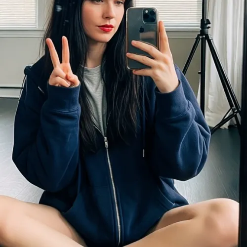 A young woman with long dark hair and bangs sits cross-legged on